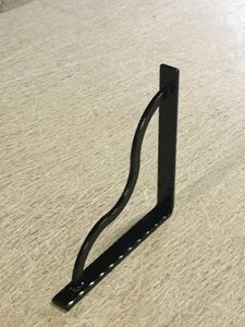 A black metal shelf bracket is sitting on a carpeted floor.
