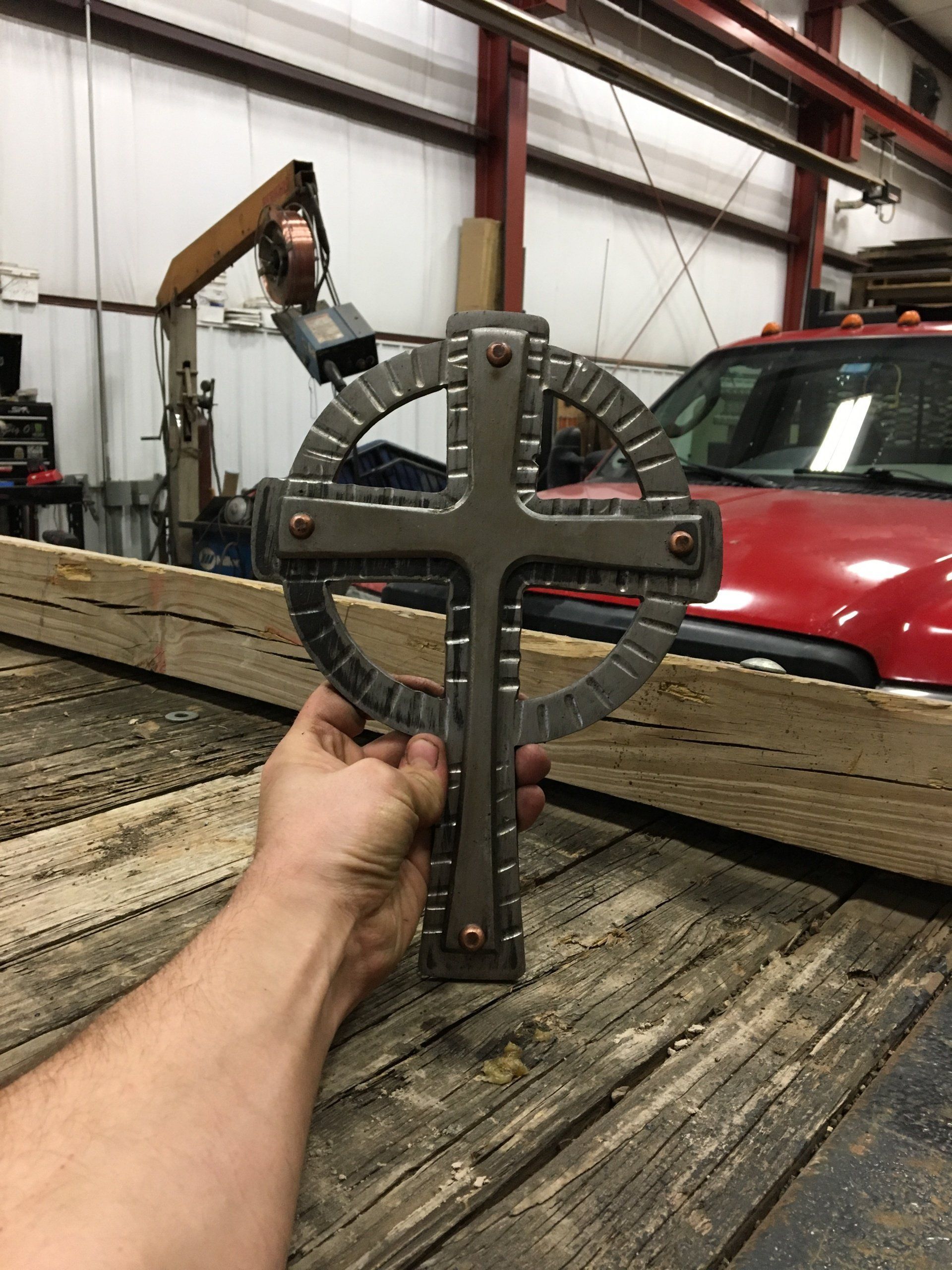 A person is holding a metal cross in front of a red truck.