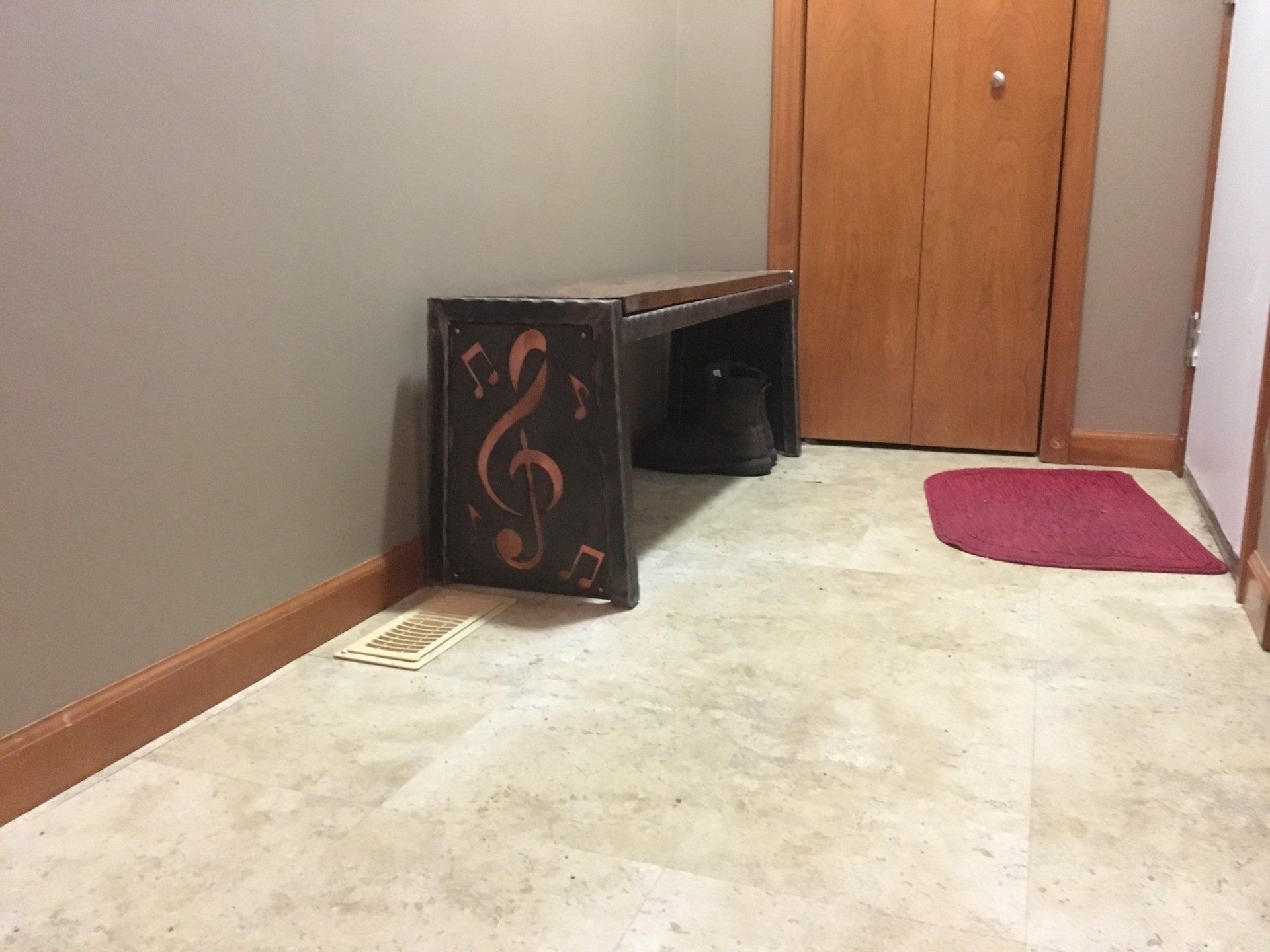 A wooden bench with a treble clef on it is in a hallway next to a door.