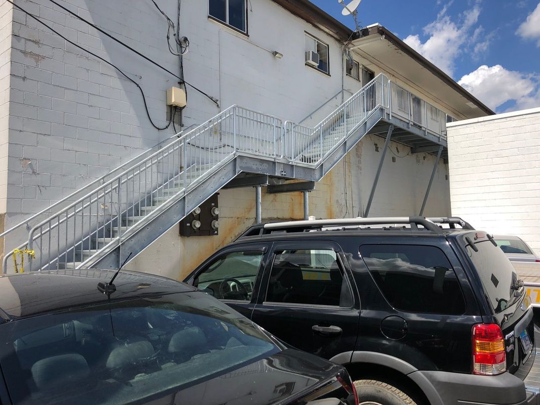 Two cars are parked in front of a building with stairs leading up to it.