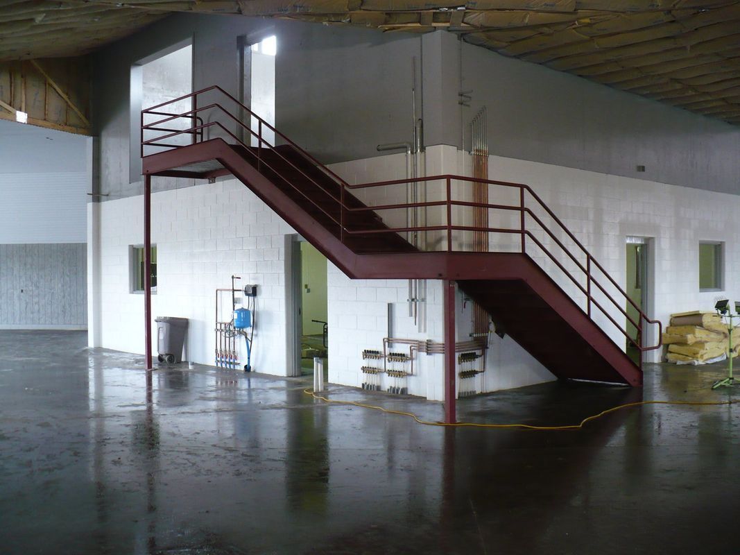 An empty warehouse with a red staircase leading up to the second floor