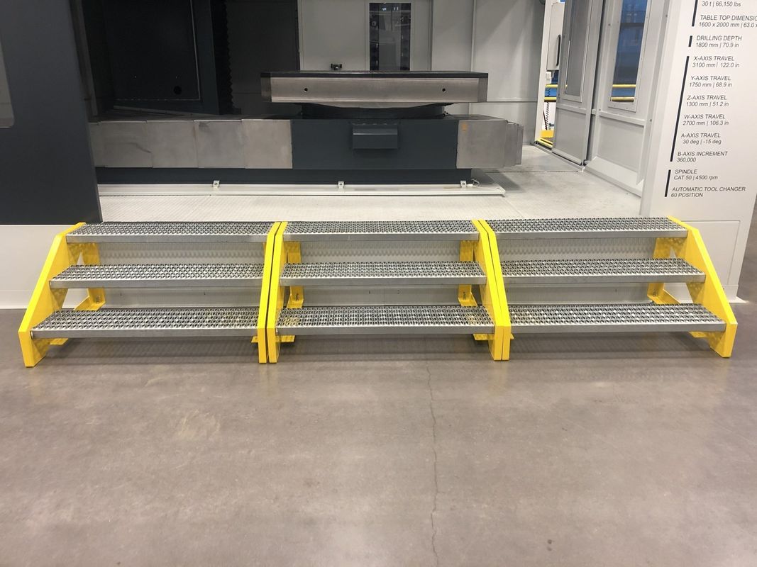 A row of metal steps with yellow handles are sitting on a tiled floor in front of a machine.