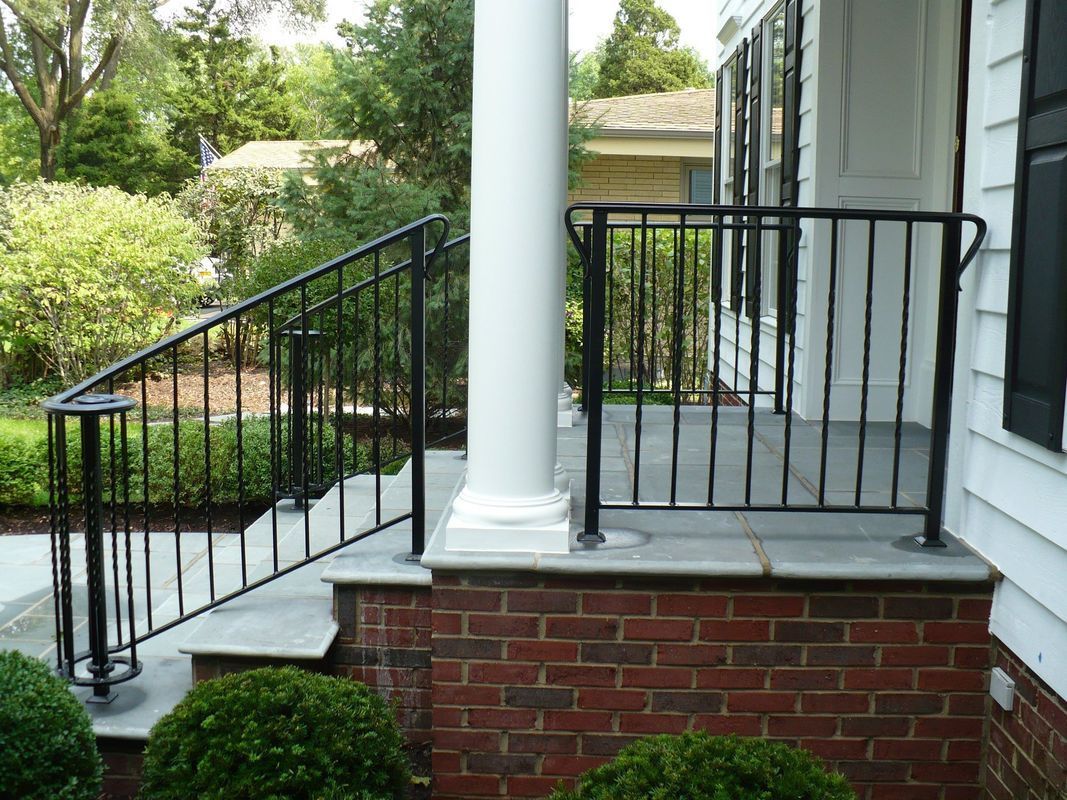 A porch with a wrought iron railing and stairs leading up to it.
