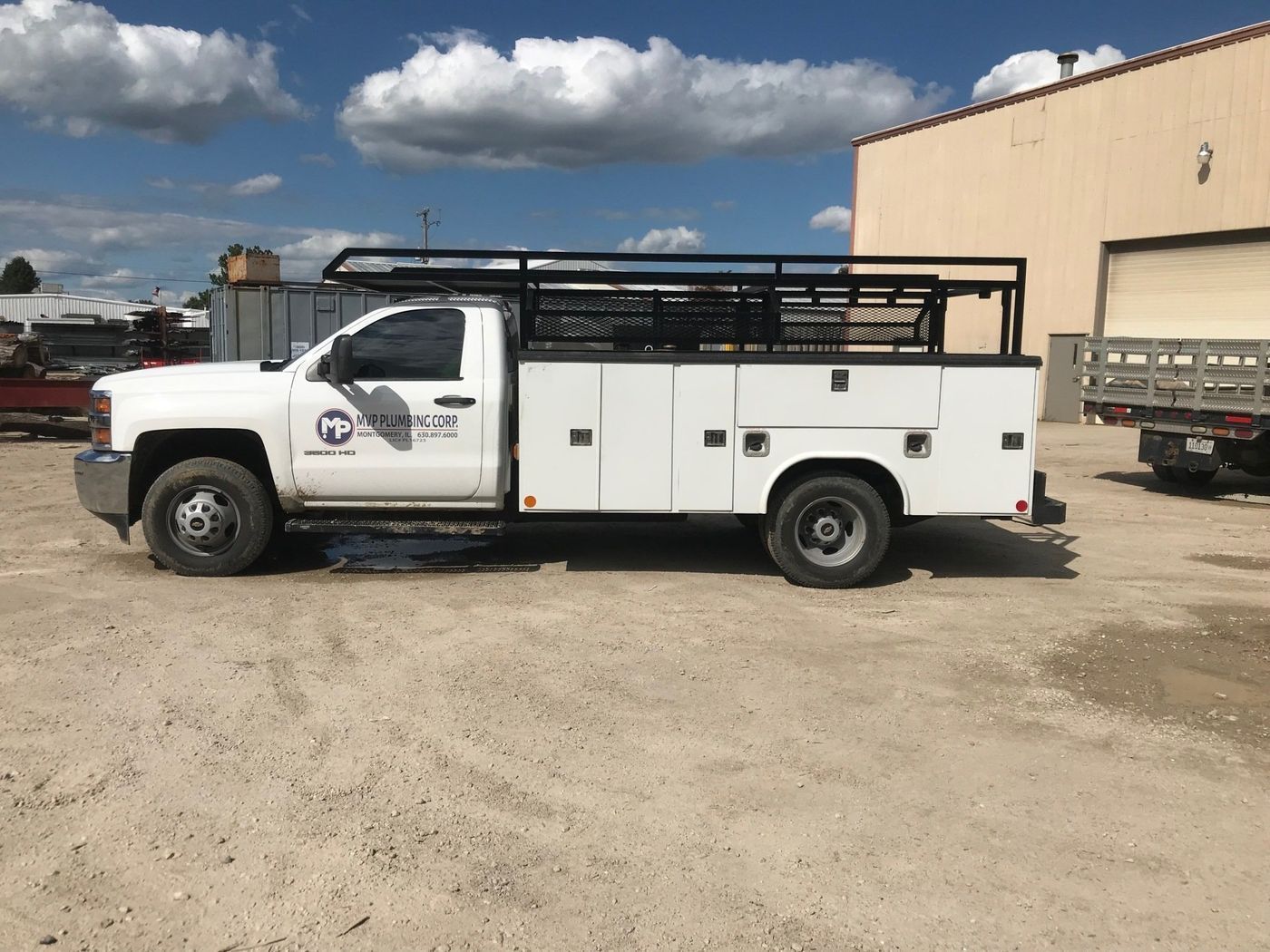 A white utility truck is parked in a dirt lot in front of a building.