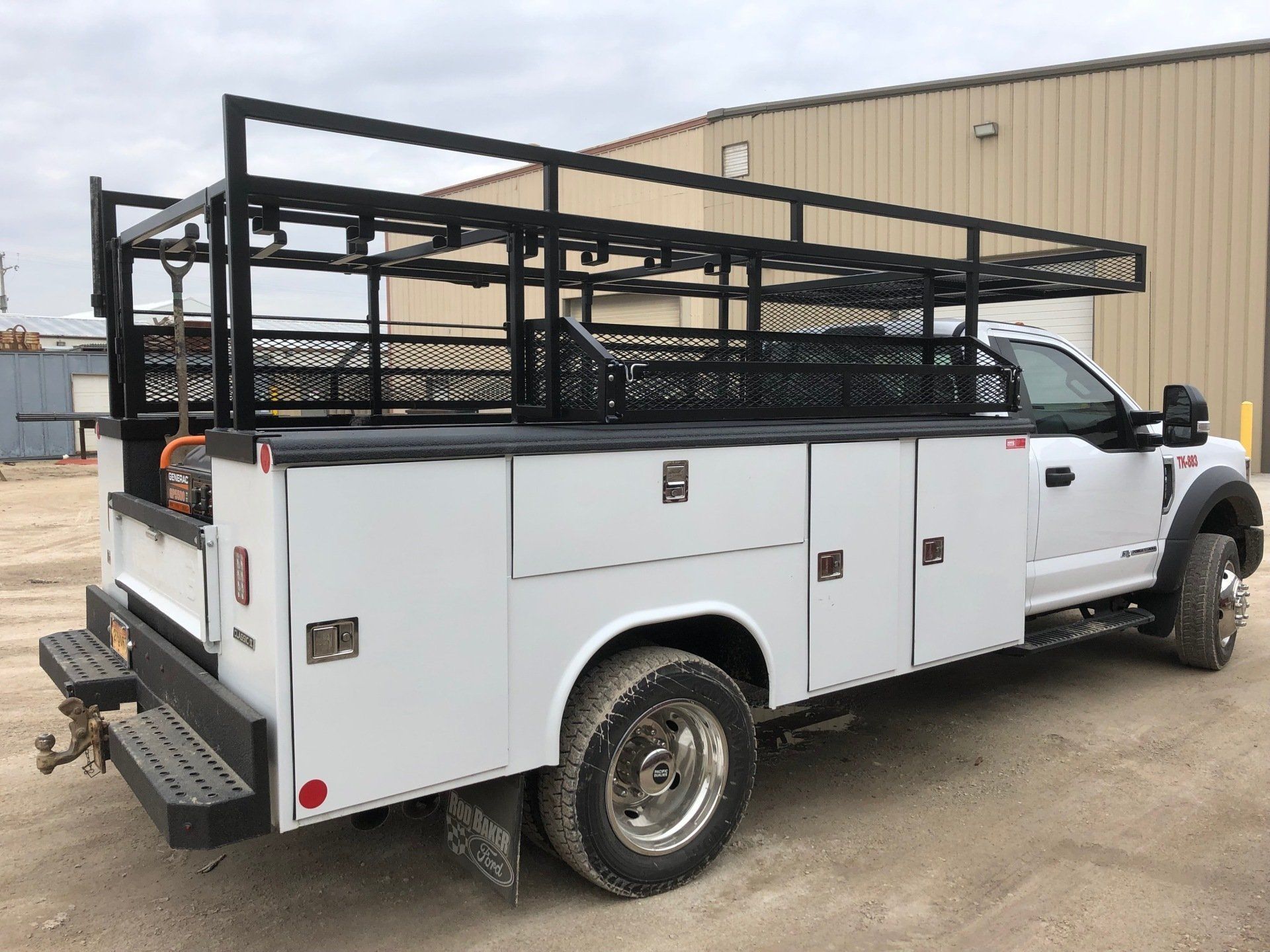 A white truck with a ladder rack on the back is parked in front of a building.