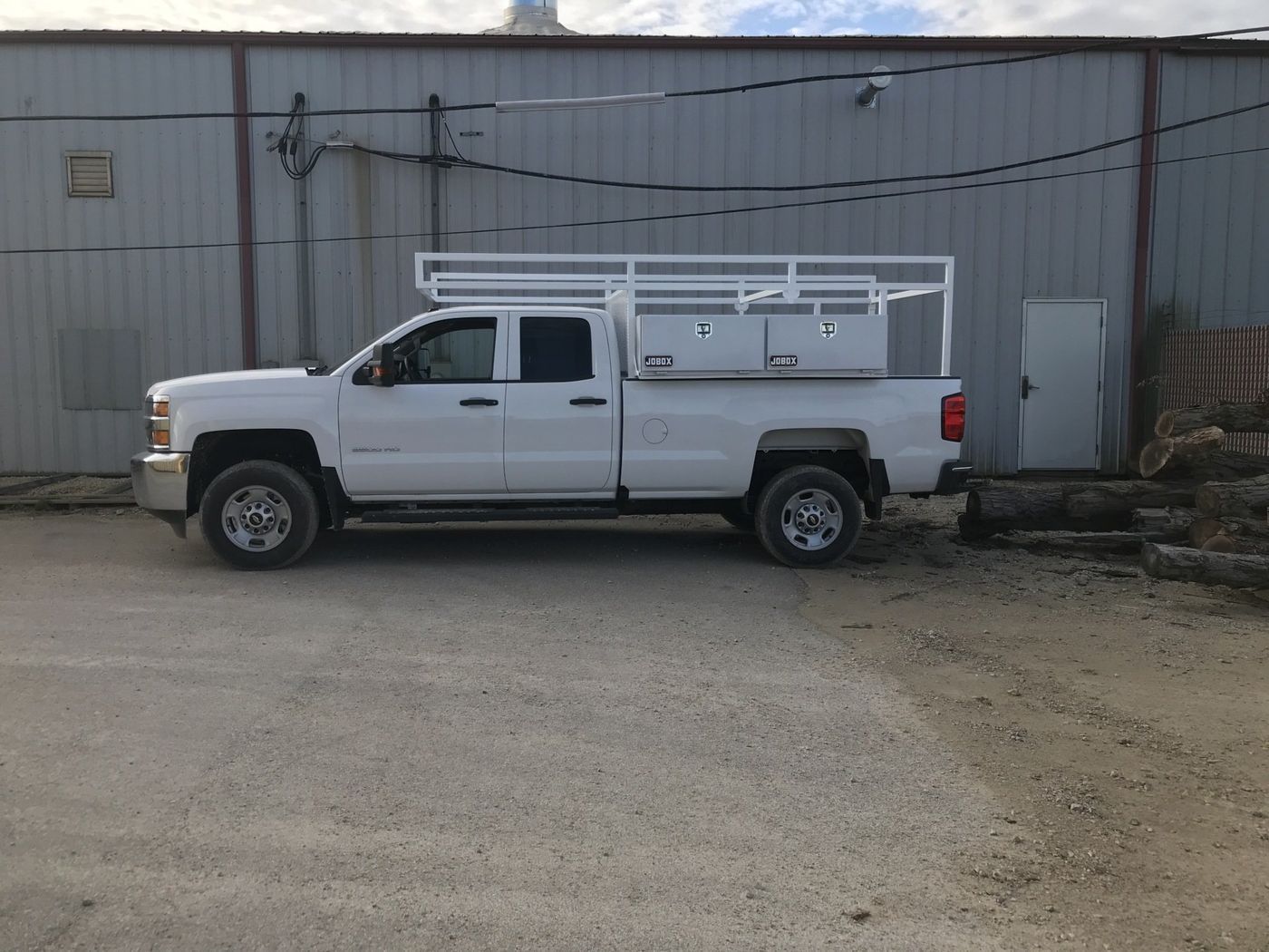 A white truck with a ladder rack on the back is parked in front of a building.