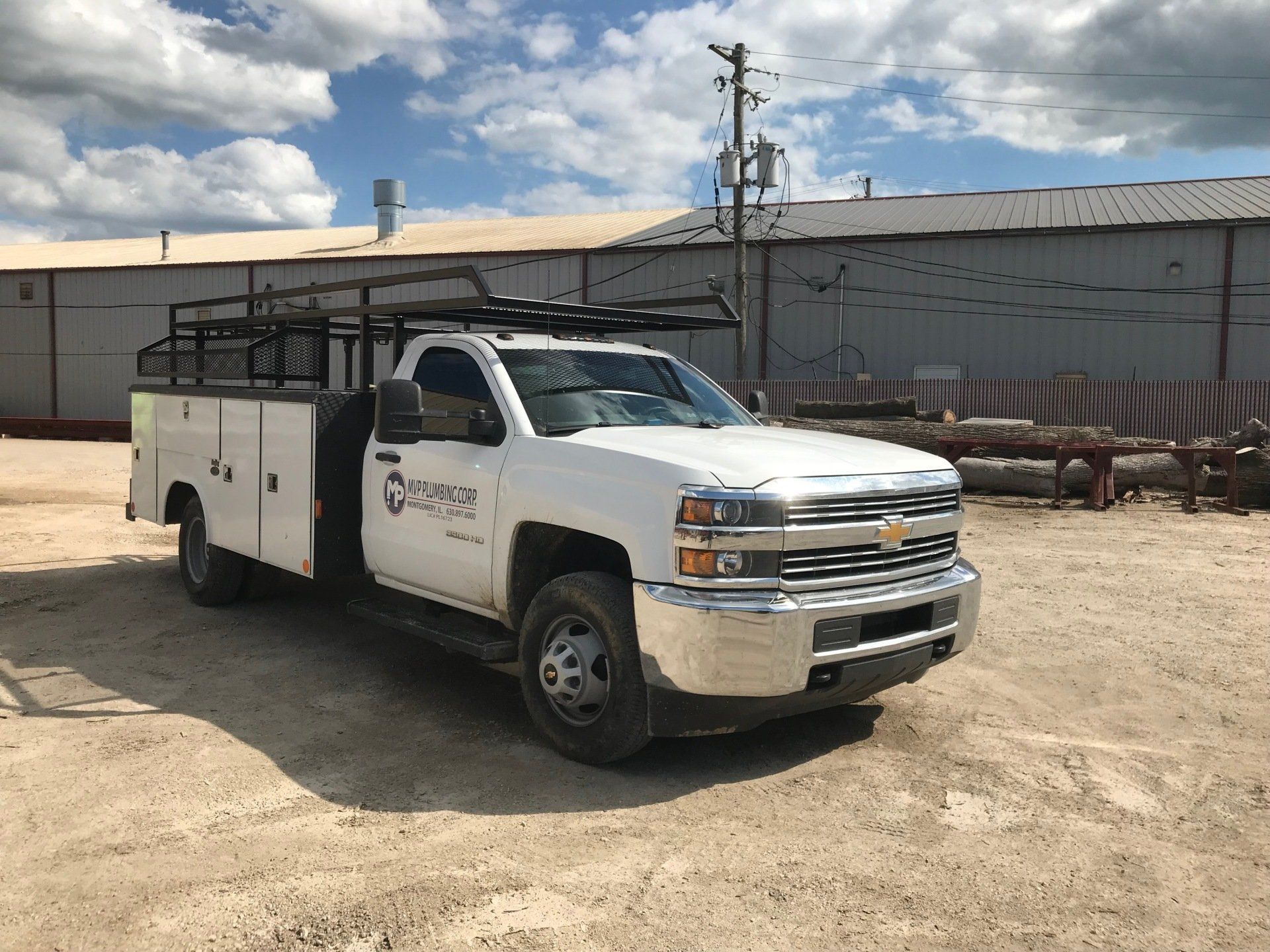 A white truck is parked in a dirt lot in front of a building.