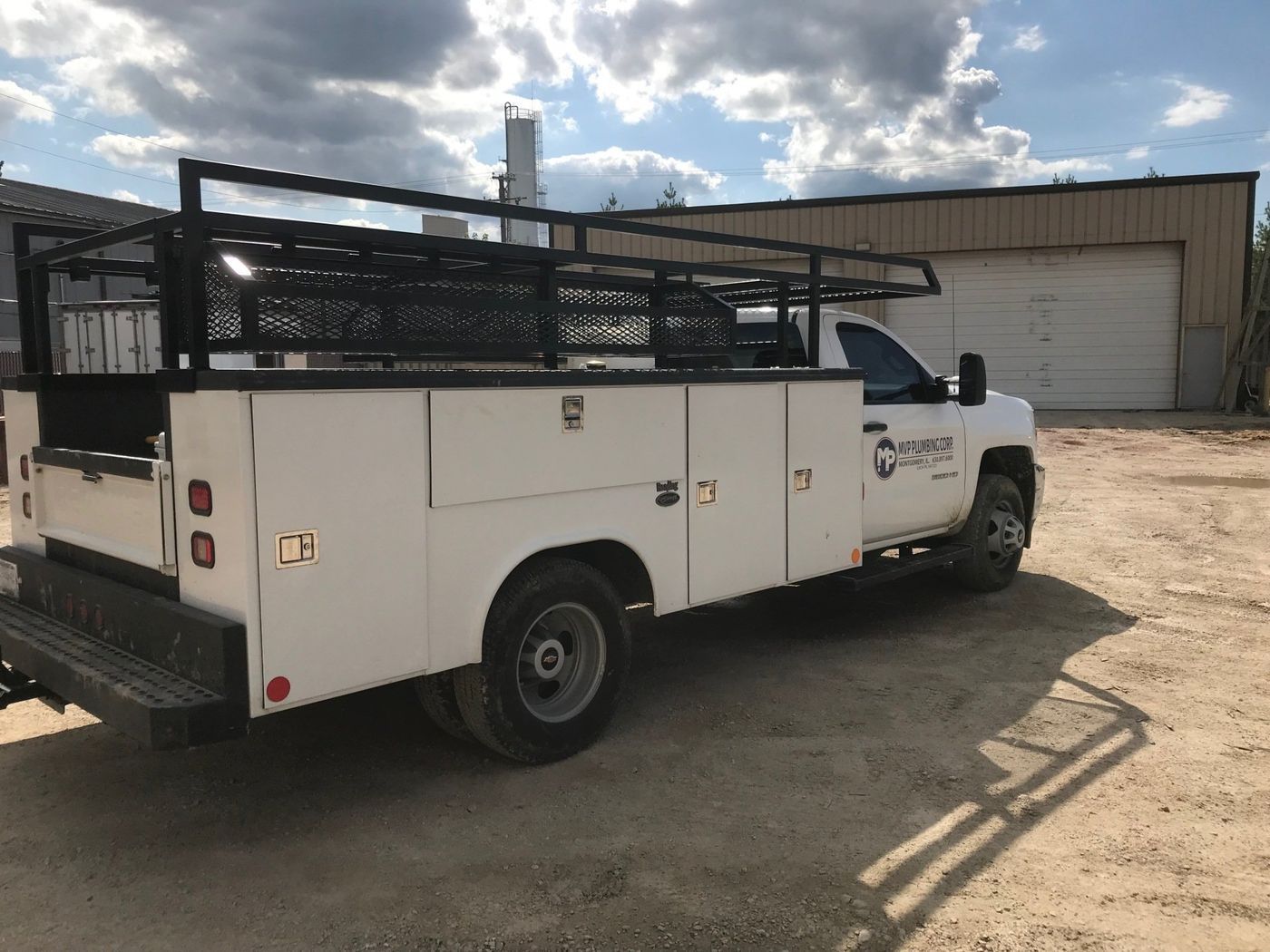 A white utility truck is parked in a dirt lot in front of a building.