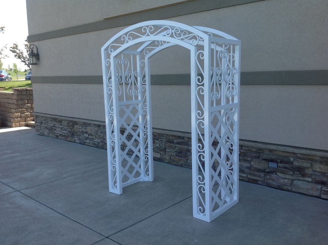 A white arch is sitting on the sidewalk in front of a building.