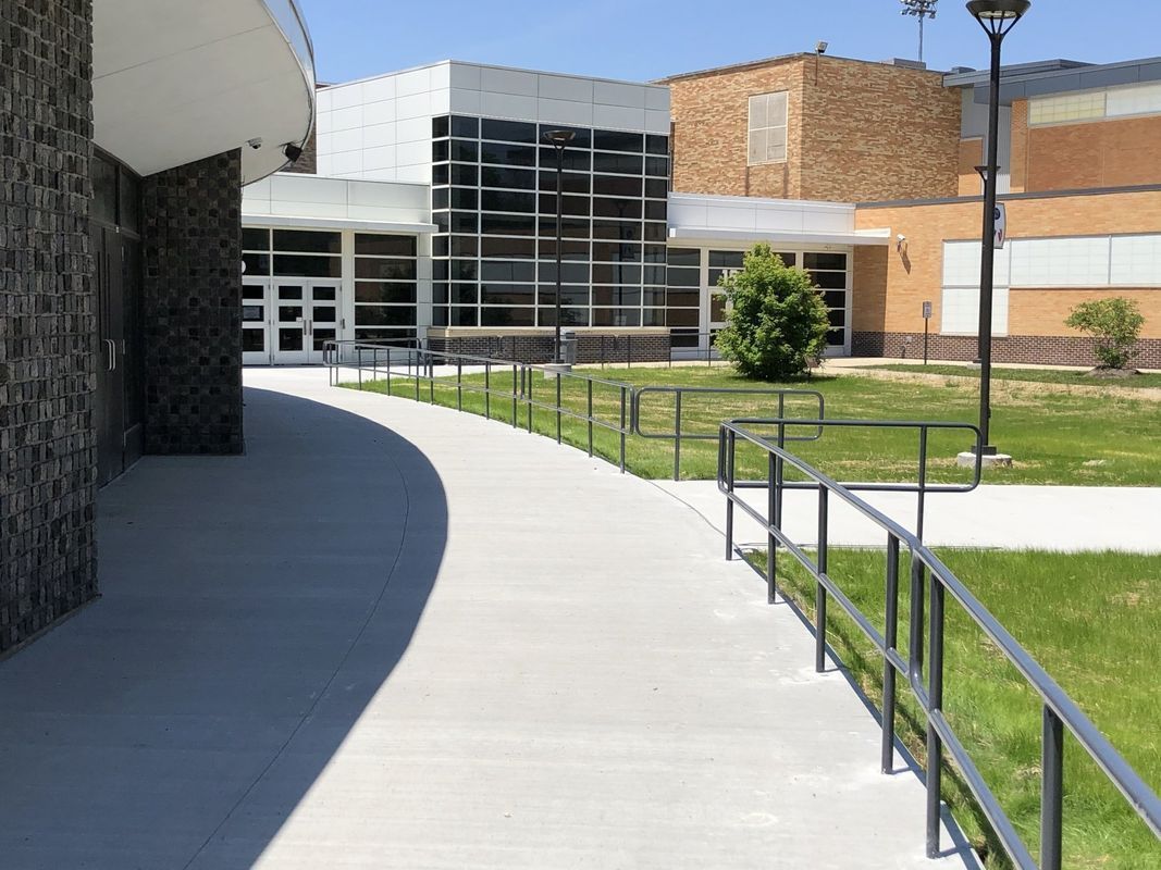 A concrete walkway leading to a large building with a railing.