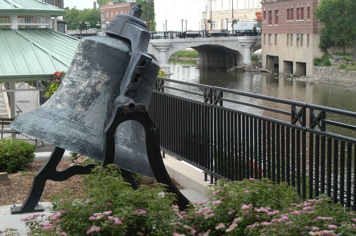 A statue of a bell with a bridge in the background