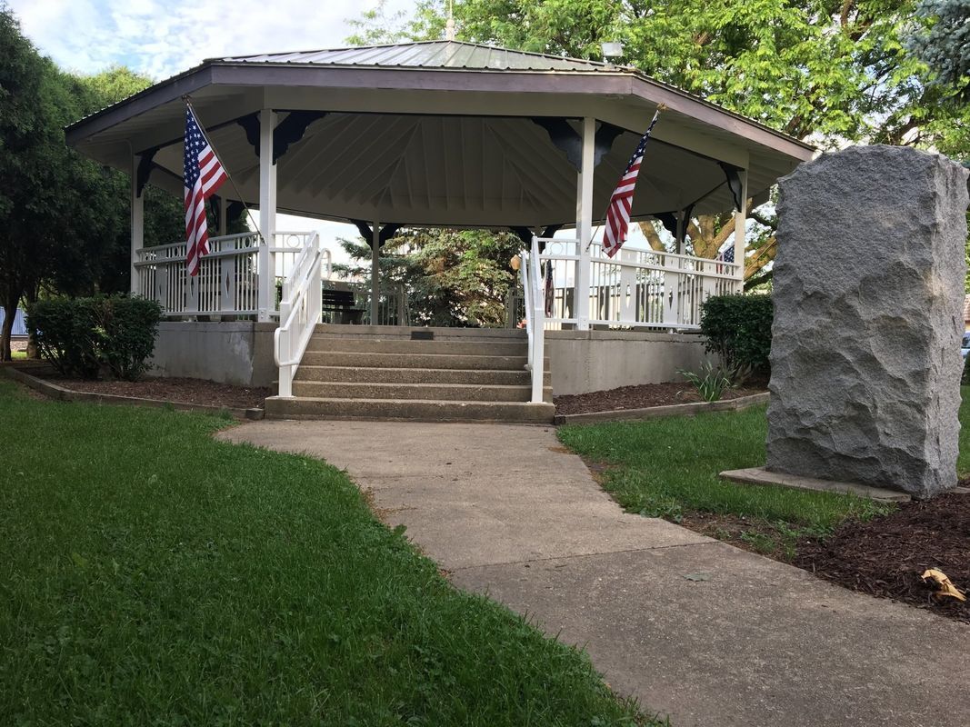 There is a gazebo in the middle of a park with american flags.
