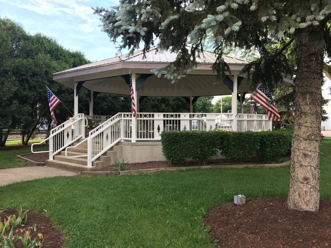 There is a gazebo in the middle of a park with stairs leading up to it.