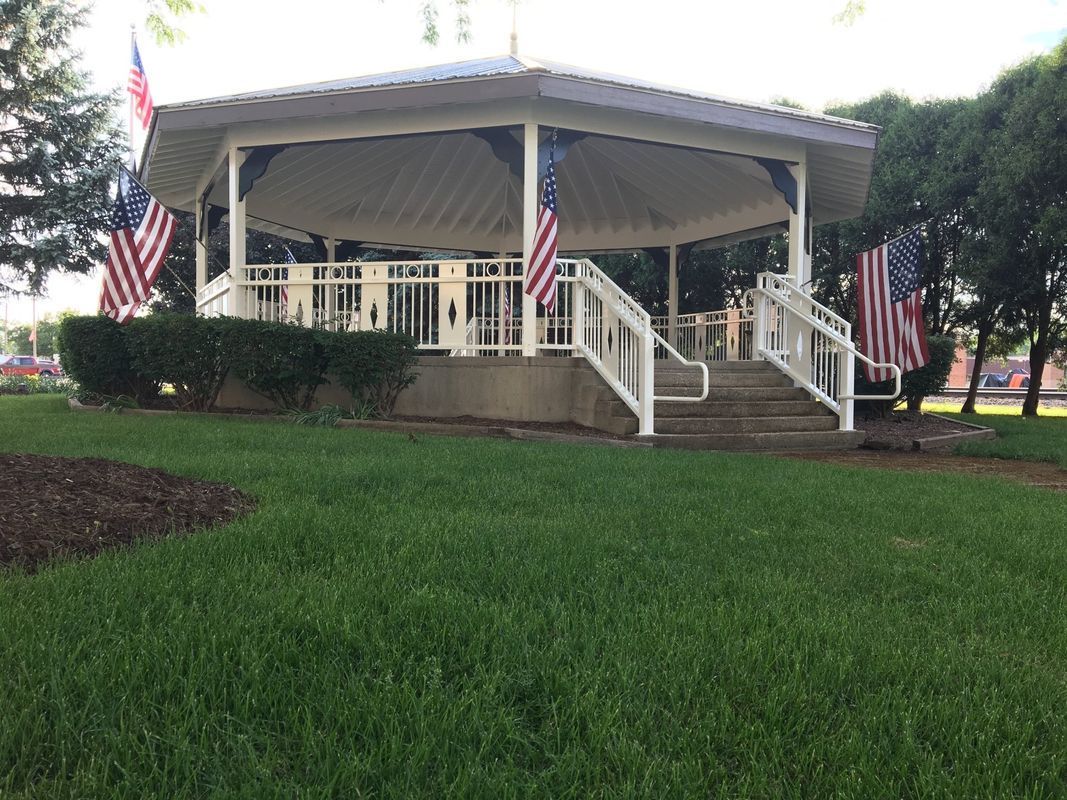 A white gazebo with stairs and american flags in a park.