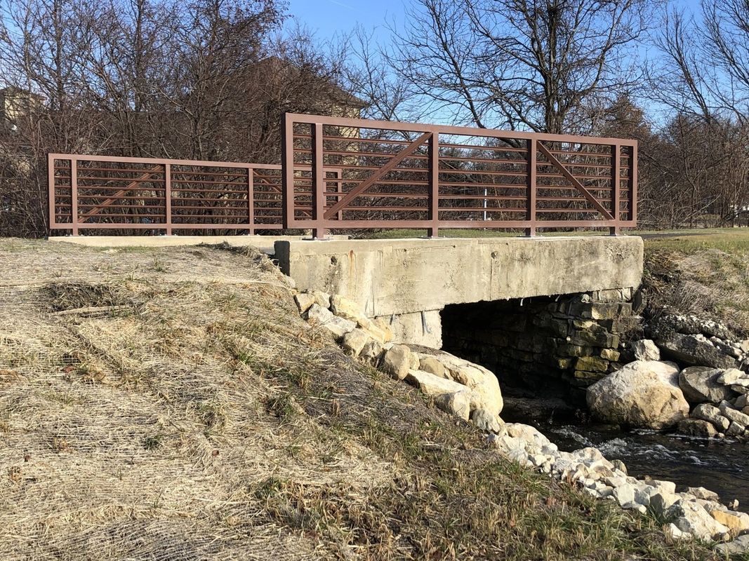 A bridge over a stream in a park with trees in the background.