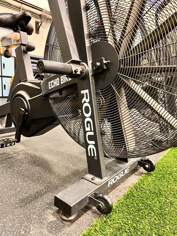 Black Rogue Echo bike with fan blades, in a gym setting, on a green turf strip.