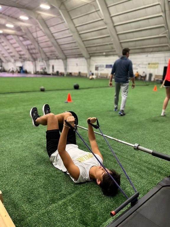 A person lying on the ground exercising with a resistance band and barbell in an indoor gym.