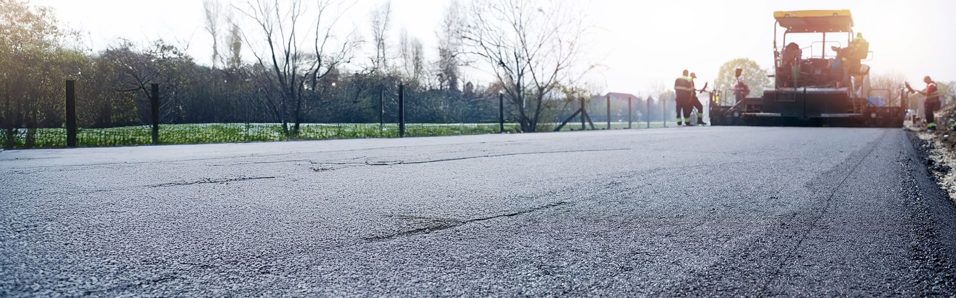 Asphalt paving in progress on a road. Workers and machinery are laying fresh asphalt.