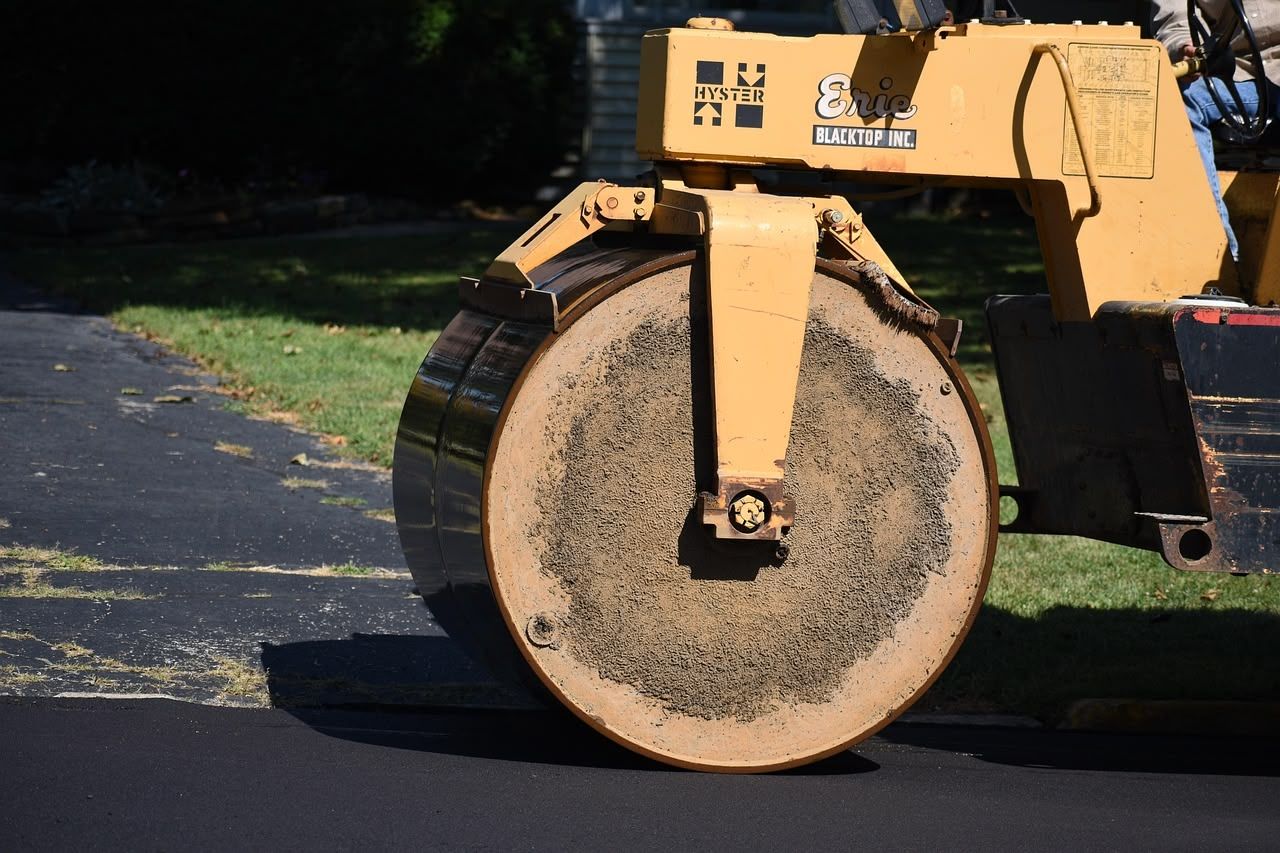 Yellow road roller compacting fresh asphalt on a driveway.
