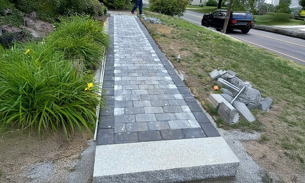 Stone walkway with dark and light gray pavers, bordered by dark gray. Steps lead up to the path.