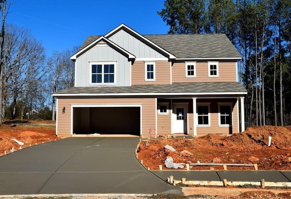 Two-story house under construction with a concrete driveway and garage; brown siding, blue sky.