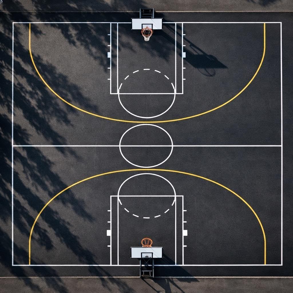 Overhead view of a basketball court with white lines, a yellow arc, and two backboards on dark asphalt.