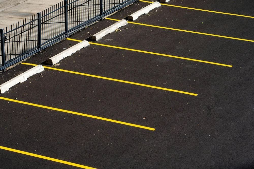 Empty parking spaces with yellow lines and wheel stops next to a black fence.