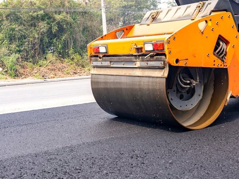Road roller compacting fresh asphalt on a road, orange and black.