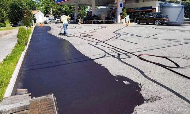 Person sealing asphalt at a gas station. Black sealant covers a large area.