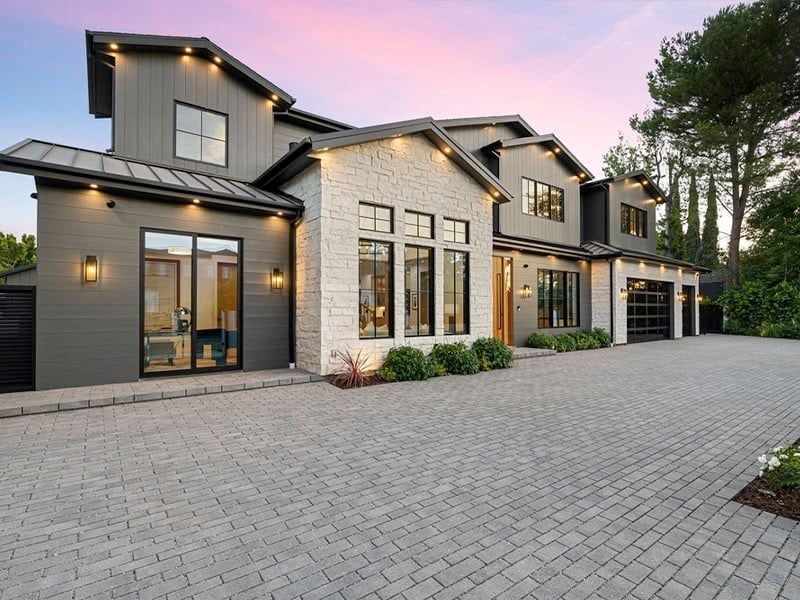 Modern gray and white house with a stone facade and paved driveway at dusk.