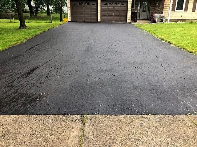 Newly paved asphalt driveway leading to a house with two garage doors; green grass on either side.