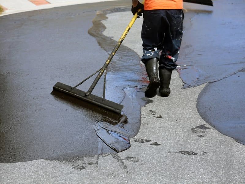 Person in boots using a broom to spread asphalt on a road.