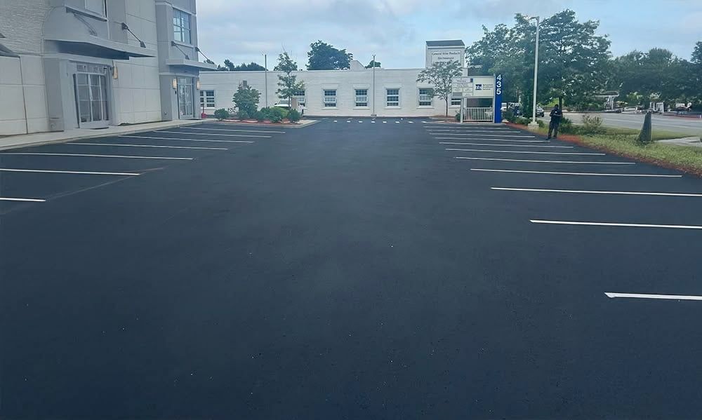 Empty, newly paved parking lot with white painted parking space markers. Buildings in the background.