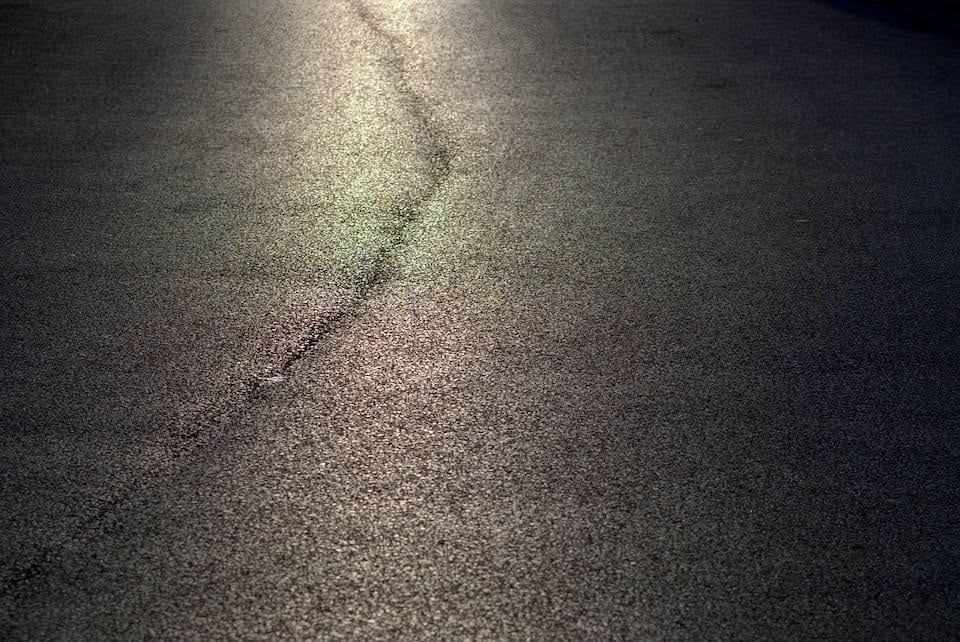 Close-up of asphalt road surface with a crack running through it, illuminated with a slight glow.