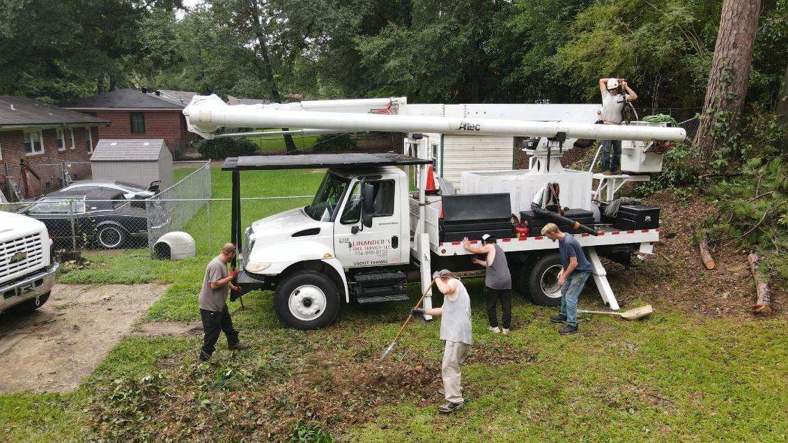Utility truck with raised boom, workers tending to equipment. Outdoors, near trees and houses.