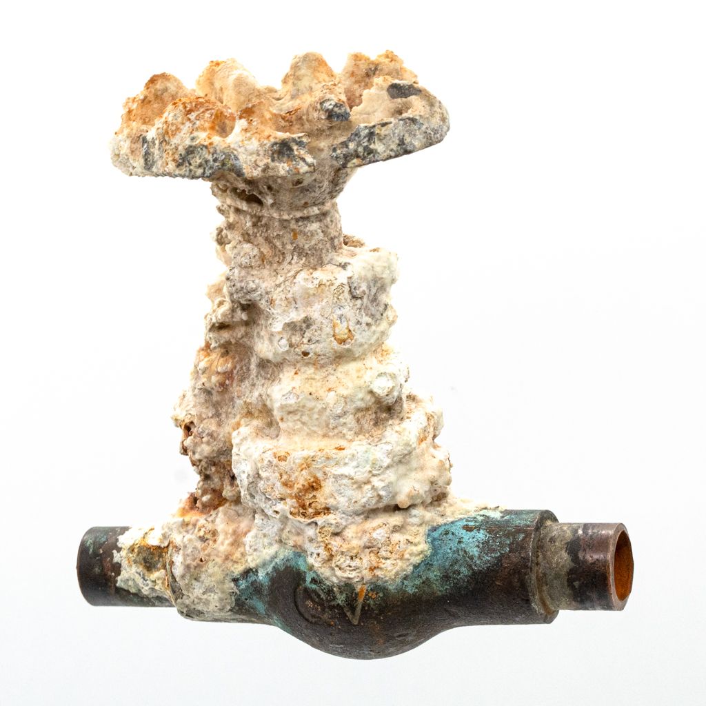 Corroded metal pipe with heavy white and orange mineral buildup and green-blue rust.