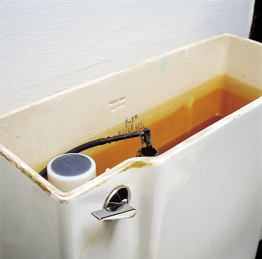 Open toilet tank with orange-tinted water and a floating black valve inside.