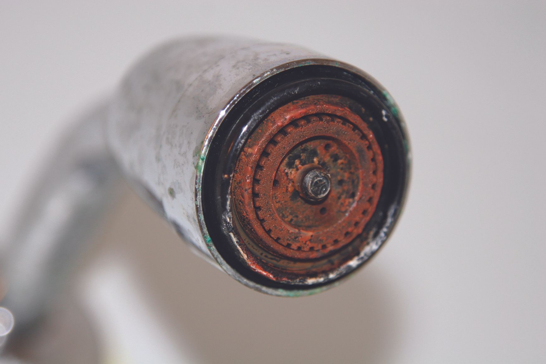 Rusty end of a metal pipe or faucet nozzle with a corroded circular opening.