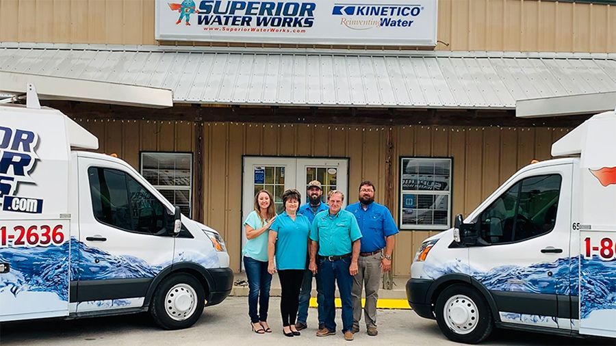 Four staff in blue shirts stand outside a business between two white service vans.