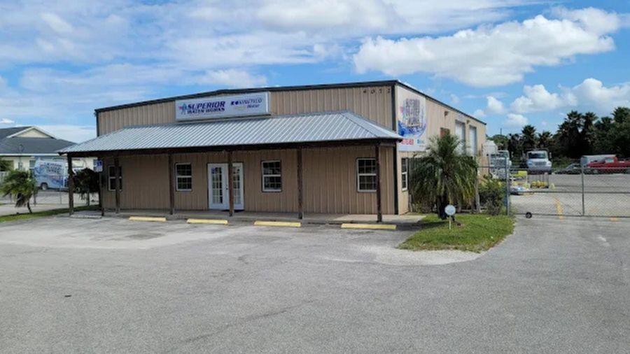 Small tan storefront with a blue awning and parking lot under a cloudy sky.