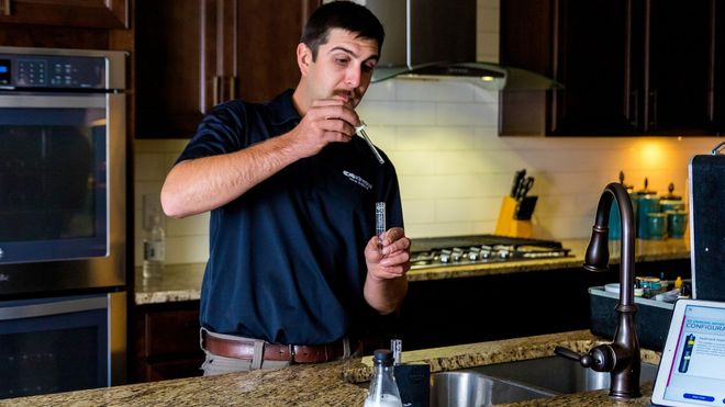 Man stirring a drink in a kitchen beside a stove and countertop electronics.