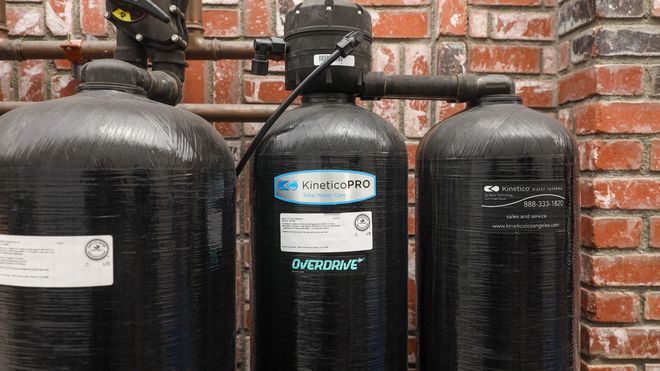 Three black water softener tanks against a red brick wall, with a central tank labeled.