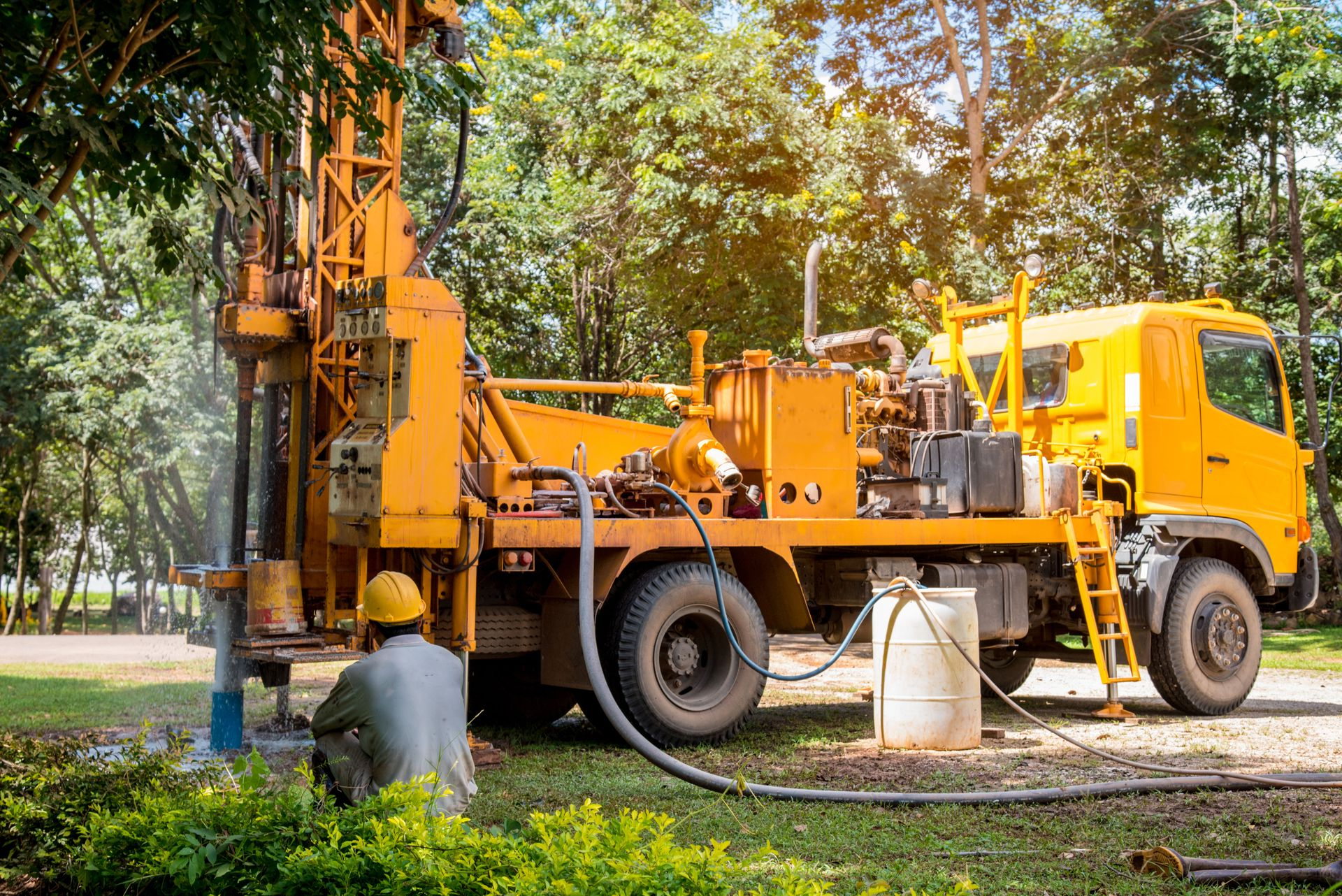 Yellow drilling truck at a wooded site with a worker operating equipment near the base.