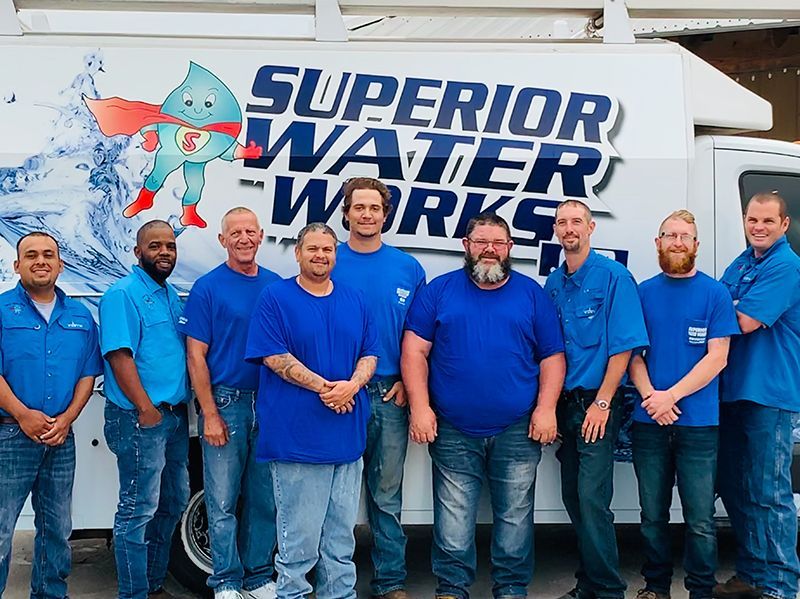Nine men in blue shirts standing in front of a Superior Water Works truck and logo.