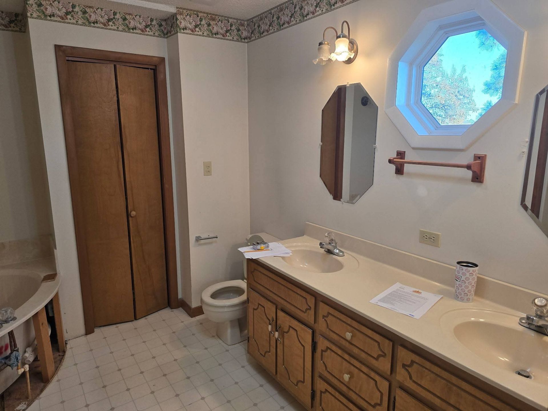 Bathroom with double vanity, octagon window, and closed closet doors.