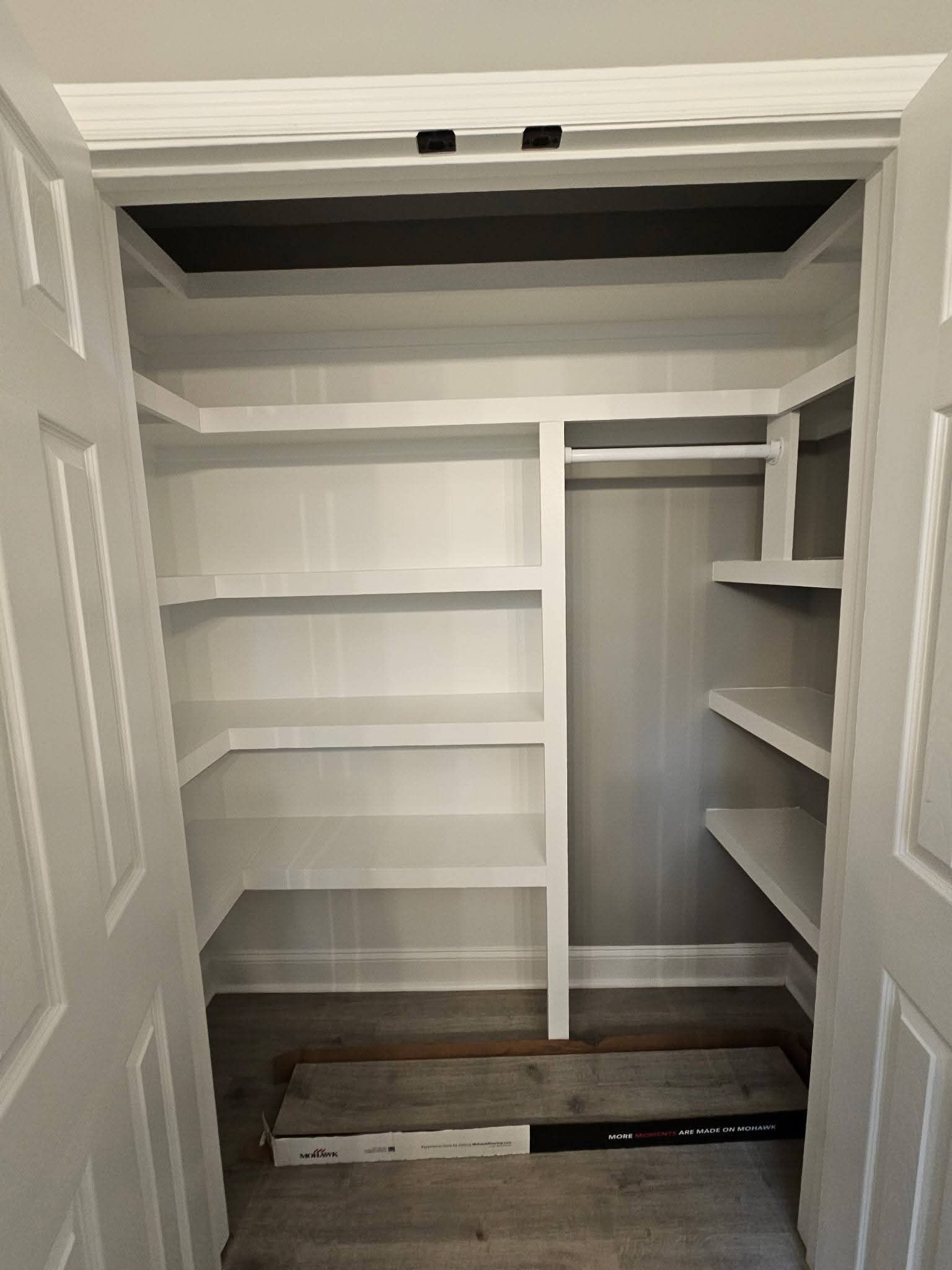White closet with built-in shelves and a hanging rod. Gray walls and wood flooring.