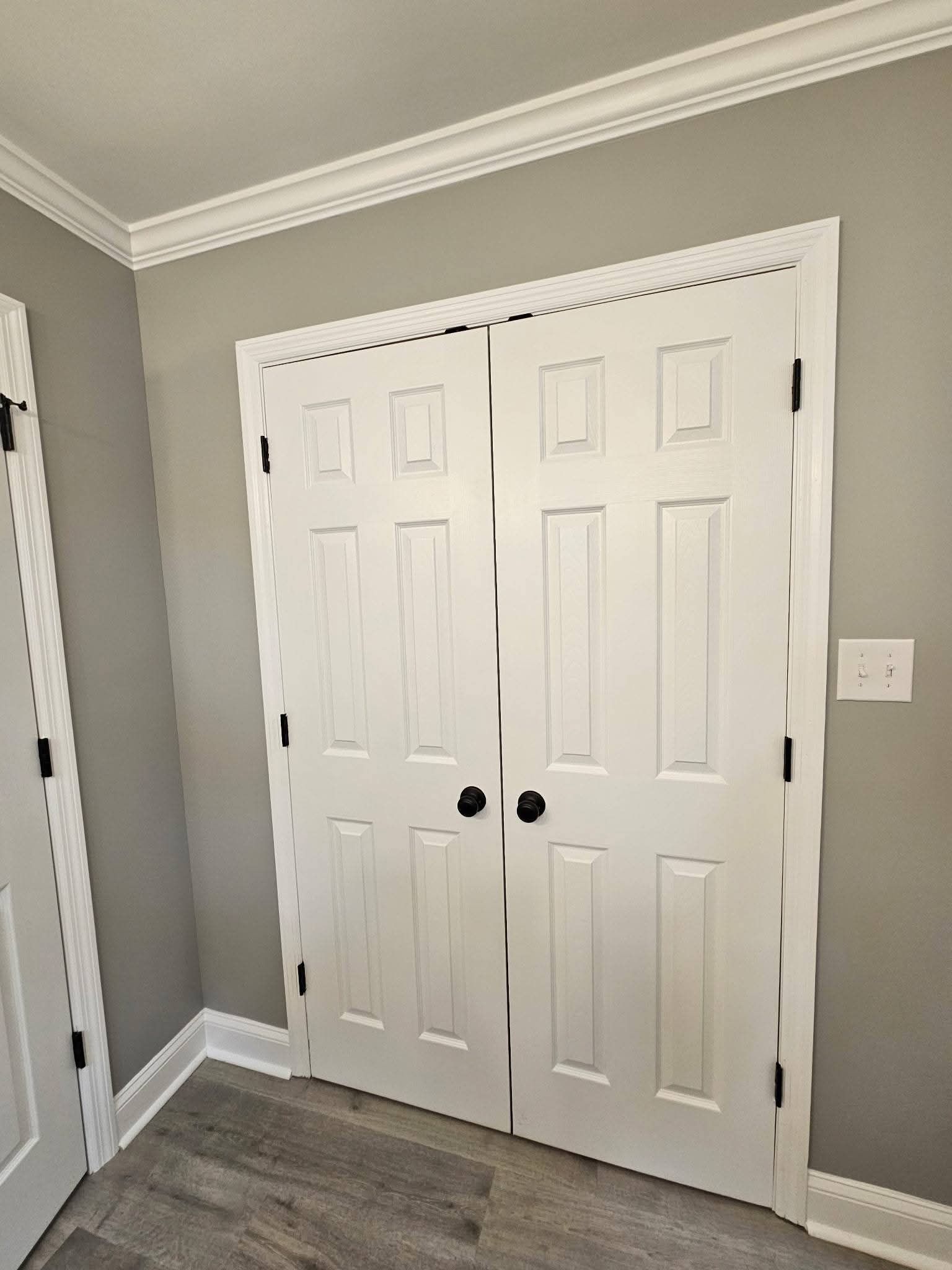 White six-panel closet doors with black hardware, surrounded by white trim and gray walls.