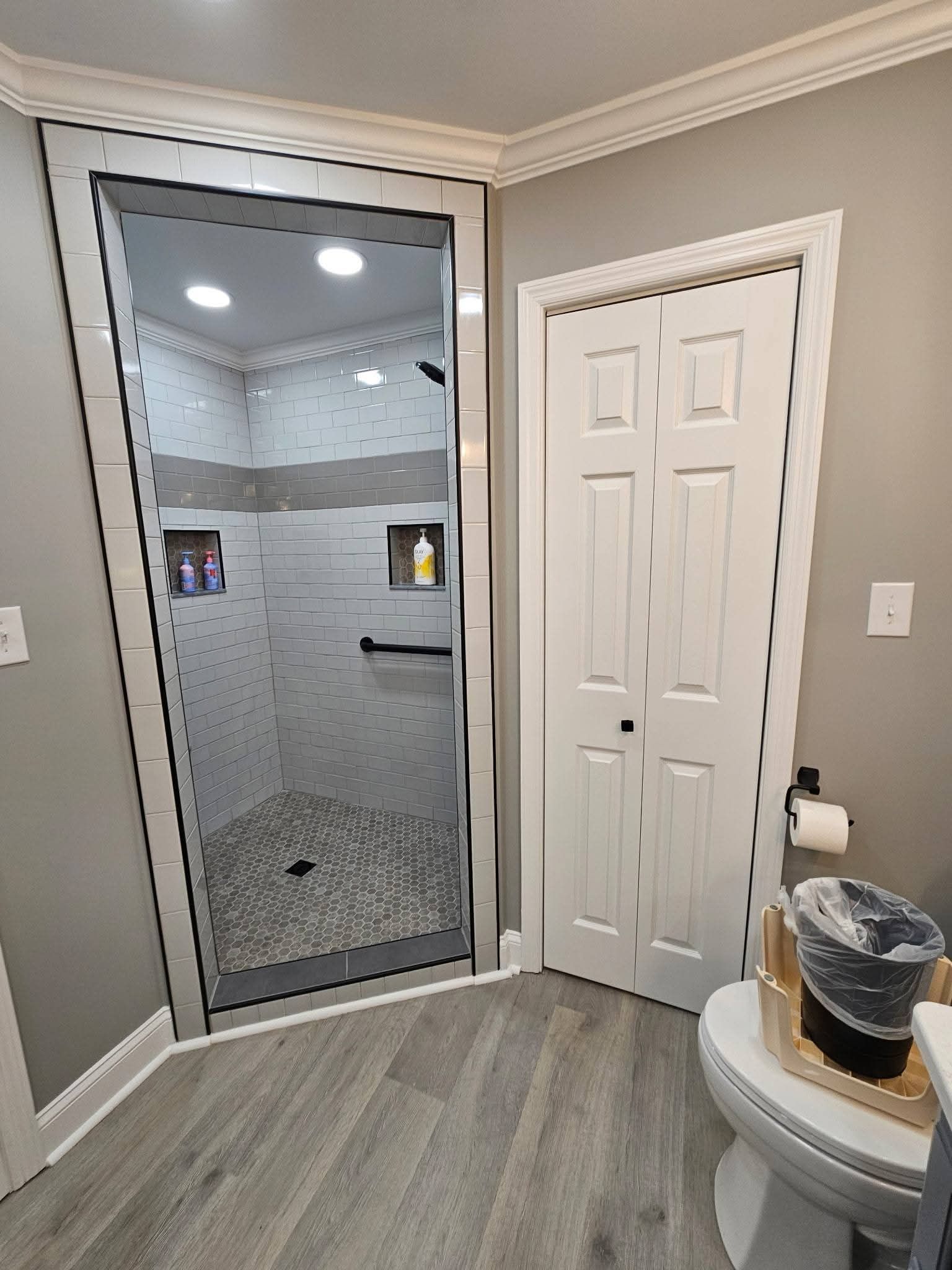 Bathroom with gray walls, a tiled shower, white door, and a toilet.