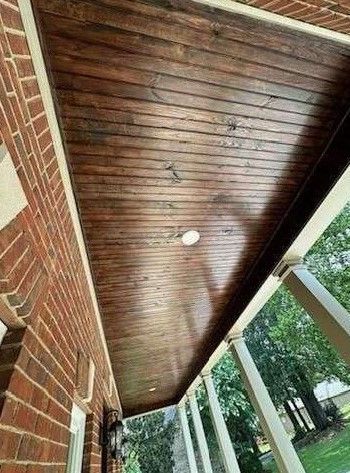 A porch with a wooden ceiling and a brick wall.