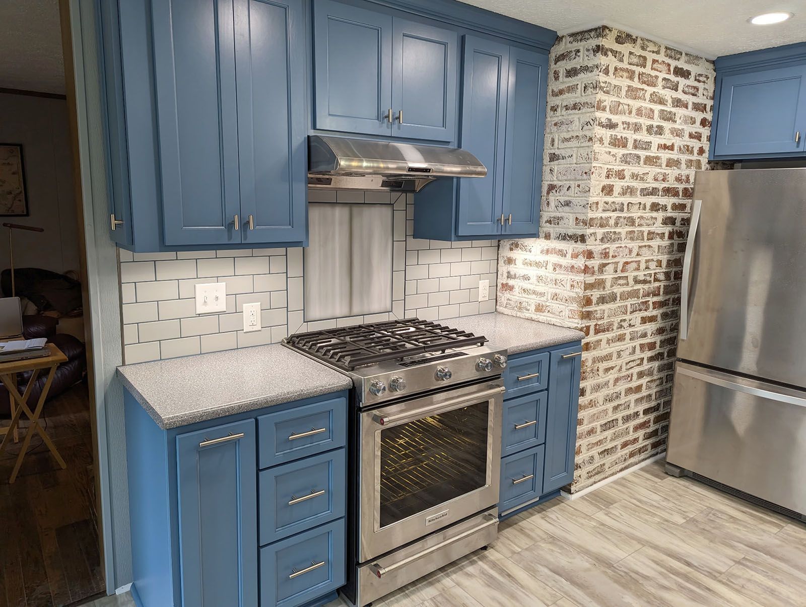 A kitchen with blue cabinets, stainless steel appliances, and a brick wall